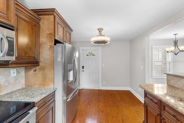 kitchen with appliances with stainless steel finishes, pendant lighting, backsplash, and light stone counters