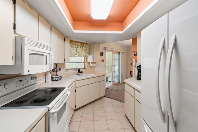 kitchen with sink, white appliances, a tray ceiling, and light tile patterned flooring