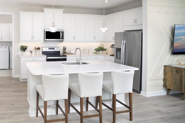 kitchen featuring stainless steel appliances, washer and dryer, a kitchen island with sink, white cabinets, and sink