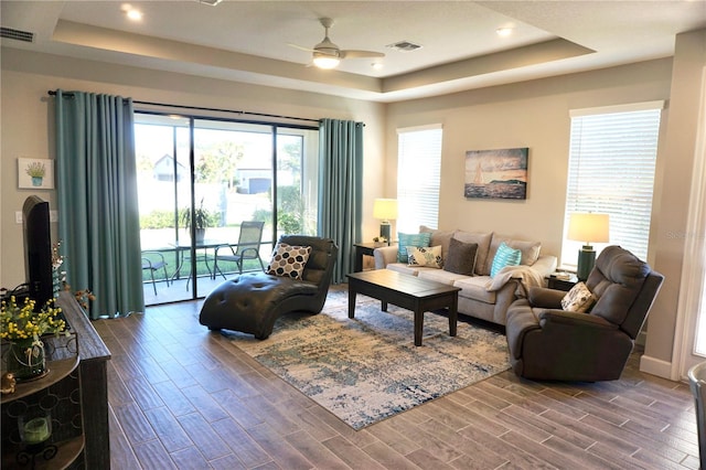 living room with a raised ceiling and ceiling fan