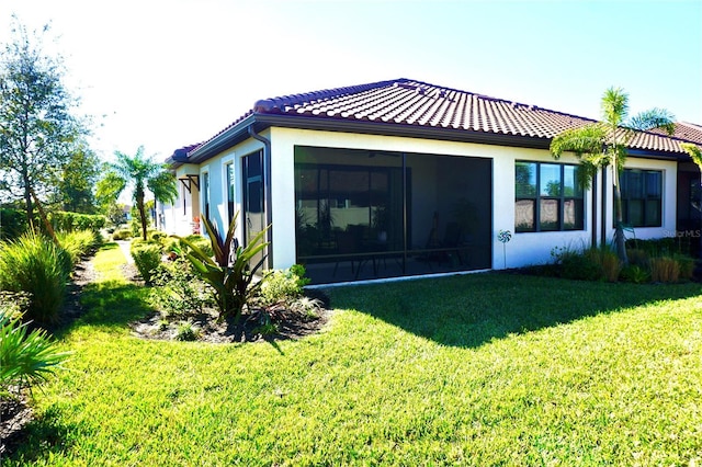 rear view of house with a yard, a tiled roof, and stucco siding