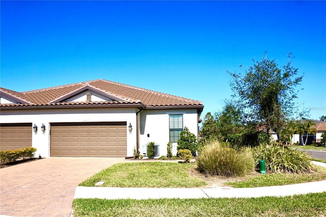 mediterranean / spanish-style home with decorative driveway, stucco siding, an attached garage, central AC, and a tiled roof