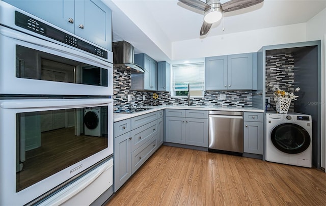 kitchen with wall chimney exhaust hood, washer / dryer, stainless steel dishwasher, double oven, and light hardwood / wood-style floors