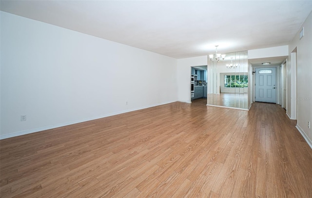 unfurnished living room with light wood-type flooring and a notable chandelier