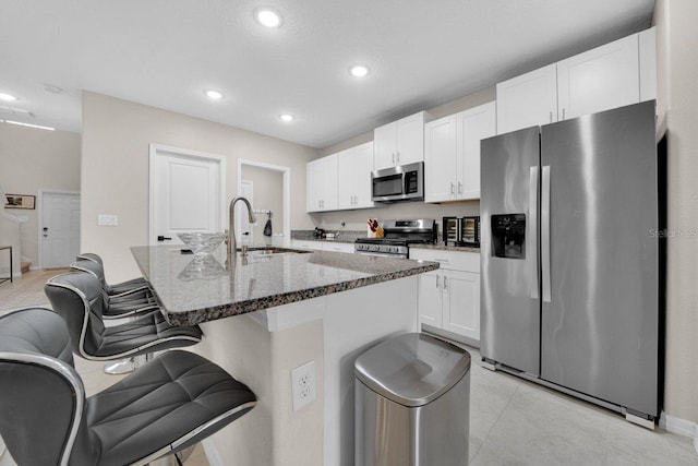 kitchen featuring a breakfast bar, sink, stainless steel appliances, white cabinets, and dark stone counters