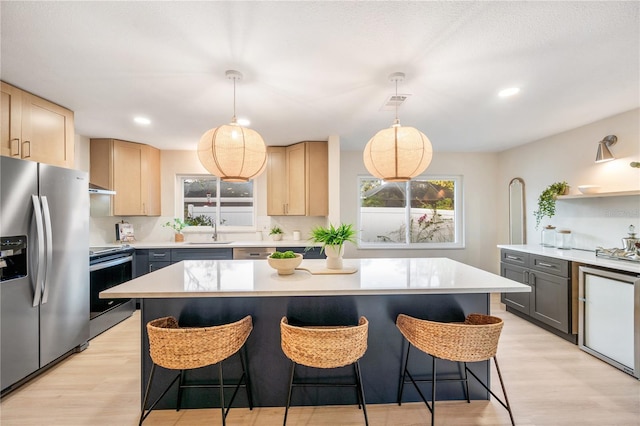 kitchen with hanging light fixtures, light brown cabinets, a center island, and stainless steel appliances