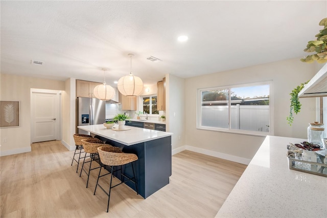 kitchen with stainless steel refrigerator with ice dispenser, light brown cabinetry, light hardwood / wood-style floors, and hanging light fixtures