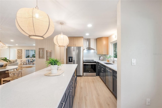 kitchen featuring stainless steel appliances, light brown cabinetry, hanging light fixtures, and wall chimney range hood