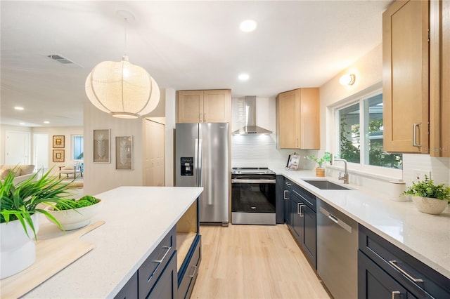 kitchen with stainless steel appliances, light brown cabinetry, wall chimney range hood, pendant lighting, and light stone counters