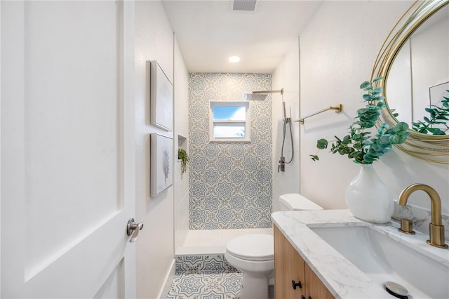 bathroom with toilet, a tile shower, tile patterned floors, and vanity