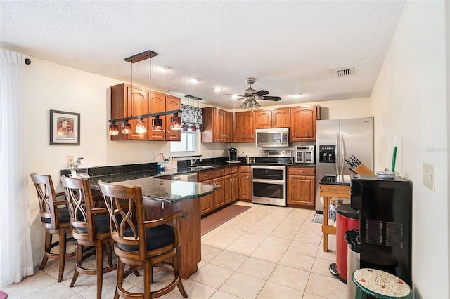 kitchen with hanging light fixtures, stainless steel appliances, kitchen peninsula, and a textured ceiling