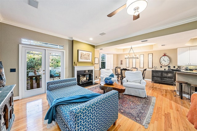 living room with french doors, ceiling fan with notable chandelier, ornamental molding, and light hardwood / wood-style floors