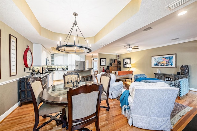 dining room with light wood-type flooring, ceiling fan with notable chandelier, and ornamental molding