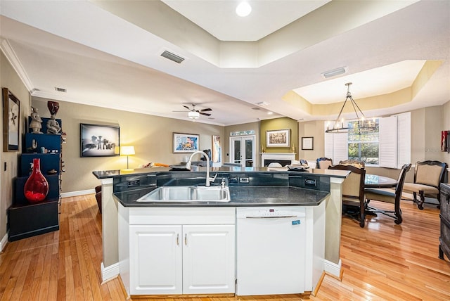 kitchen featuring an island with sink, a tray ceiling, white dishwasher, ceiling fan with notable chandelier, and sink