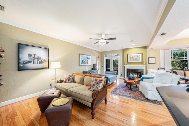 living room featuring ceiling fan, a tile fireplace, ornamental molding, and light hardwood / wood-style floors