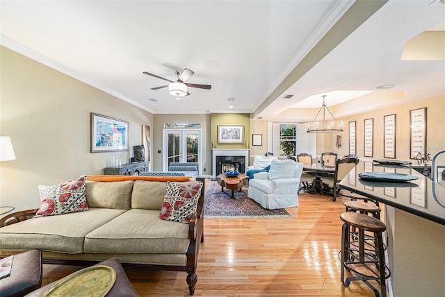 living room featuring a tray ceiling, ceiling fan with notable chandelier, ornamental molding, and light hardwood / wood-style floors