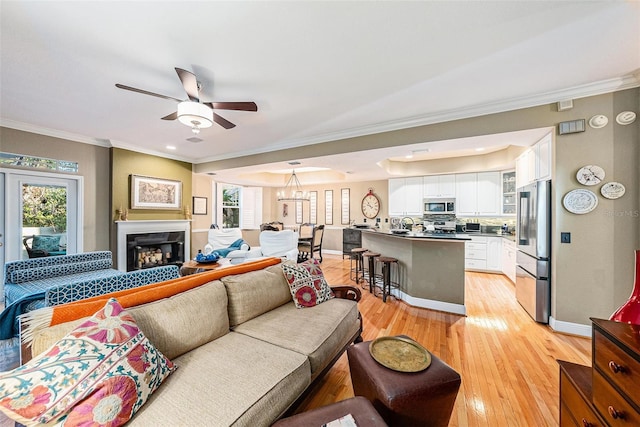 living room with light wood-type flooring, ornamental molding, and ceiling fan with notable chandelier