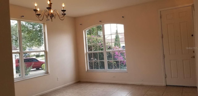 tiled spare room with a healthy amount of sunlight and a notable chandelier