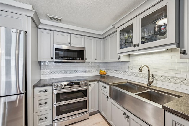 kitchen with stainless steel appliances, sink, a textured ceiling, and gray cabinetry