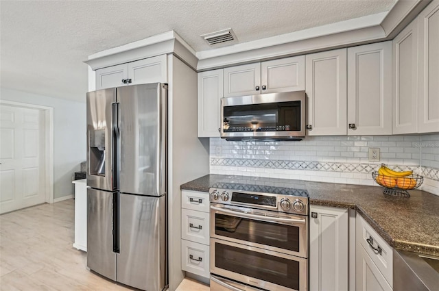 kitchen with gray cabinetry, backsplash, stainless steel appliances, and dark stone counters