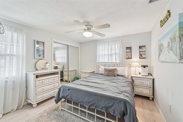 bedroom with a closet, a textured ceiling, ceiling fan, and light hardwood / wood-style flooring