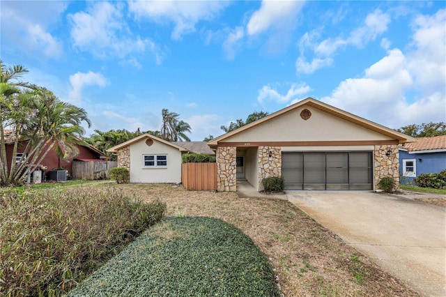 ranch-style home featuring concrete driveway, stone siding, an attached garage, central AC, and stucco siding