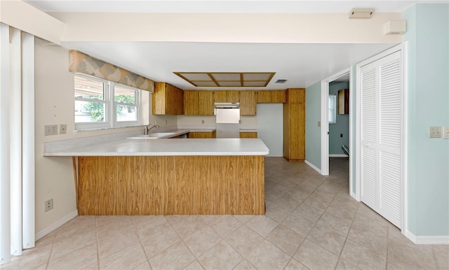 kitchen featuring brown cabinets, light countertops, a sink, a peninsula, and baseboards