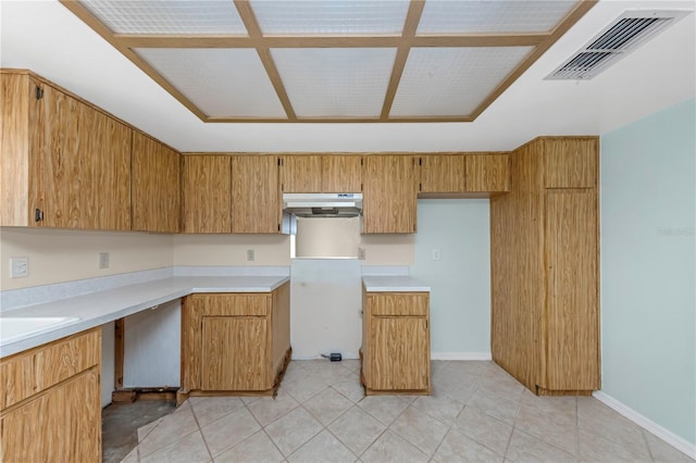 kitchen with light countertops, brown cabinetry, visible vents, and under cabinet range hood