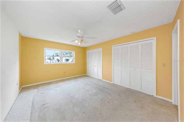 unfurnished bedroom with light carpet, visible vents, a ceiling fan, a textured ceiling, and two closets