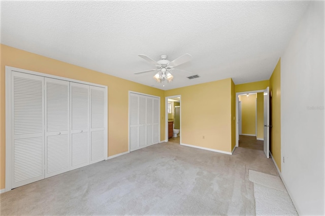 unfurnished bedroom with baseboards, visible vents, light colored carpet, a textured ceiling, and multiple closets