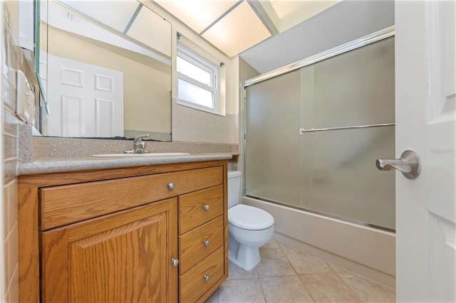 bathroom featuring toilet, bath / shower combo with glass door, tile patterned flooring, and vanity