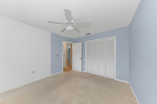 unfurnished bedroom featuring a textured ceiling, light carpet, visible vents, baseboards, and a closet