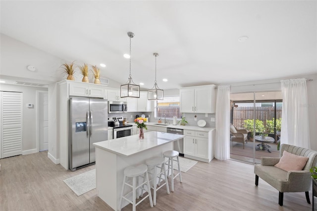 kitchen with appliances with stainless steel finishes, tasteful backsplash, white cabinets, a kitchen island, and decorative light fixtures