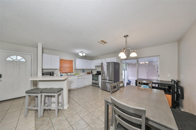 kitchen with a textured ceiling, white cabinetry, stainless steel appliances, hanging light fixtures, and light tile patterned floors