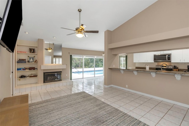 unfurnished living room with ceiling fan, light tile patterned floors, a tile fireplace, and high vaulted ceiling