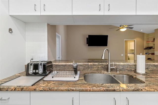 kitchen with white cabinets, built in shelves, dark stone counters, sink, and ceiling fan