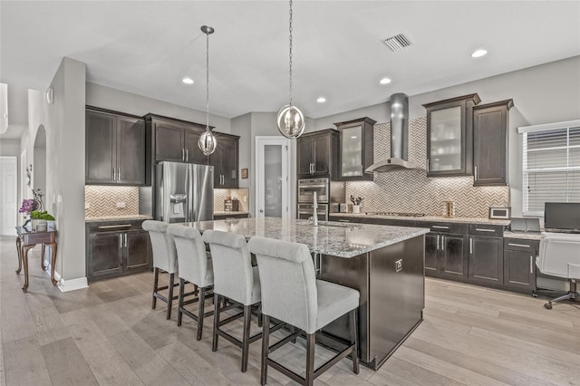 6307 Brevada Ln, Apollo Beach, FL 33572 - kitchen with wall chimney range hood, appliances with stainless steel finishes, decorative backsplash, a center island with sink, and a kitchen bar