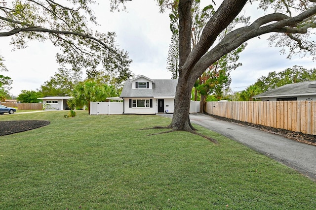 new england style home featuring driveway, a front lawn, and fence