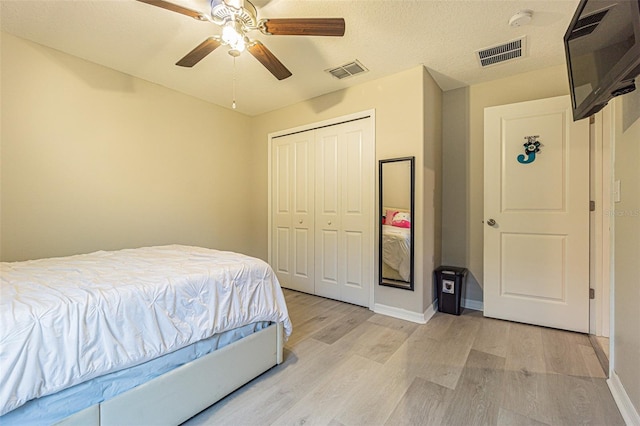 bedroom with light wood-type flooring, ceiling fan, a closet, and a textured ceiling