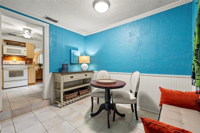 tiled dining room with ceiling fan, crown molding, and a textured ceiling