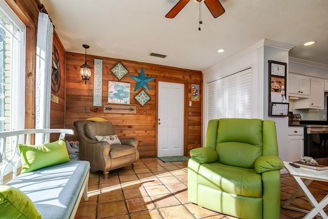 living area with ceiling fan, wooden walls, and ornamental molding