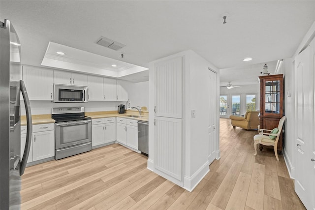 kitchen with a raised ceiling, sink, white cabinets, stainless steel appliances, and light wood-type flooring