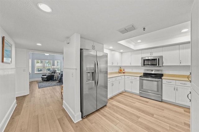 kitchen featuring appliances with stainless steel finishes, white cabinets, ornamental molding, light hardwood / wood-style floors, and a raised ceiling