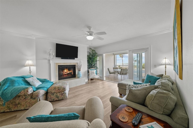 living room with a tiled fireplace, light hardwood / wood-style flooring, ornamental molding, and ceiling fan