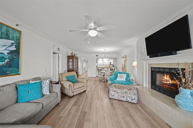 living room with a fireplace, light hardwood / wood-style flooring, ornamental molding, and ceiling fan