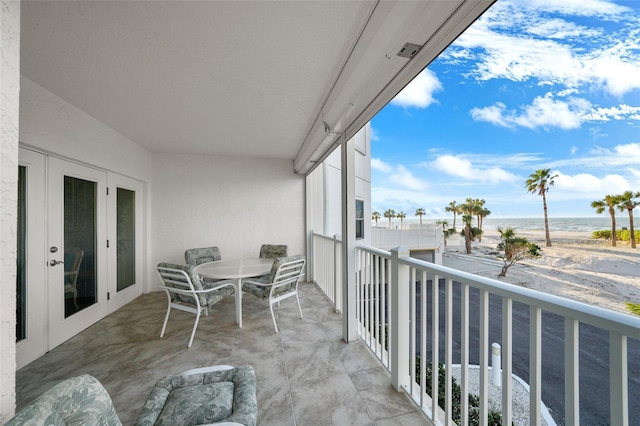 balcony with a water view, a beach view, and french doors