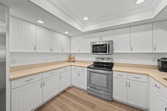 kitchen with stainless steel appliances, ornamental molding, white cabinets, and a tray ceiling