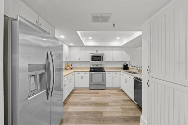 kitchen featuring appliances with stainless steel finishes, white cabinetry, ornamental molding, a raised ceiling, and light wood-type flooring