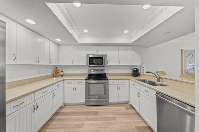 kitchen with sink, appliances with stainless steel finishes, a tray ceiling, kitchen peninsula, and white cabinets