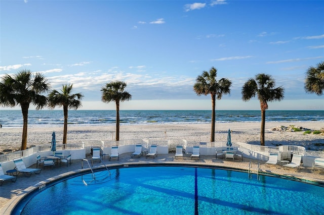 view of swimming pool featuring a water view, a view of the beach, and a patio area